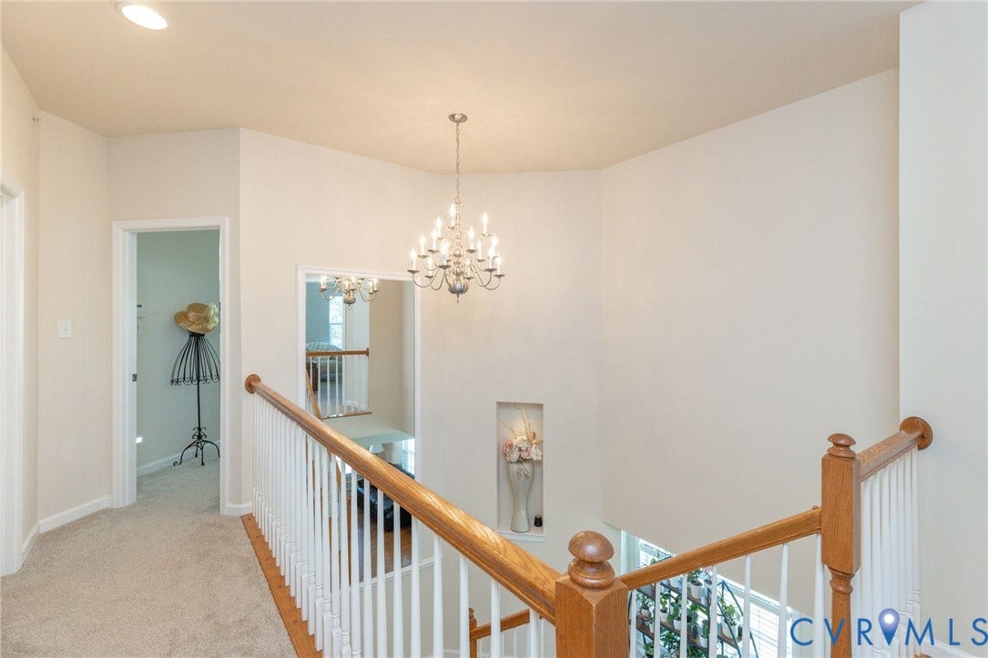 Vaulted ceiling with a chandelier light fixture, recessed lighting, carpeted hallway, wood handrail, and a wall niche