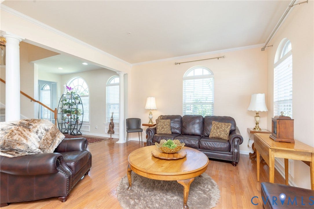 Arched windows, crown molding, wood-finish flooring, and architectural columns define this living space