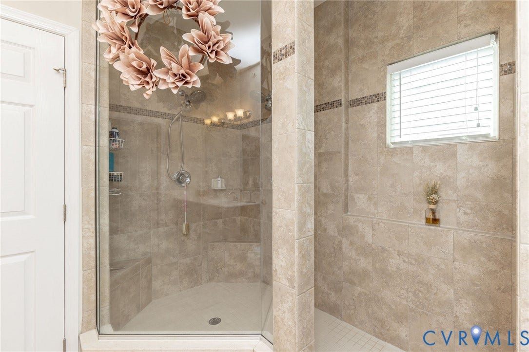 Tiled shower enclosure featuring a glass door, built-in bench, and a window with blinds