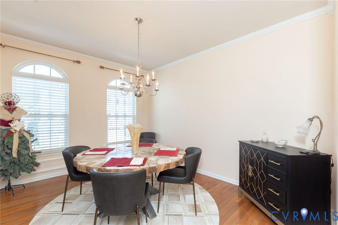 Hardwood flooring, arched windows, crown molding, and a chandelier with multiple candelabra bulbs