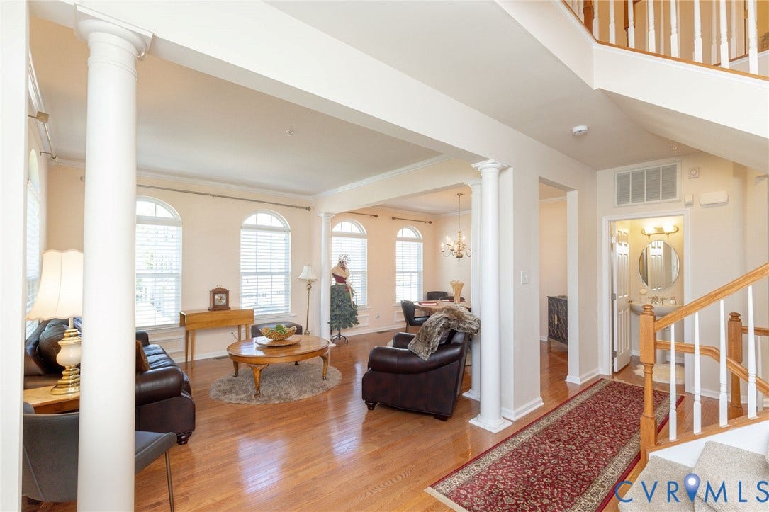 Hardwood flooring throughout, architectural columns, arched windows with blinds, a built-in pedestal sink, and a multi-tiered staircase