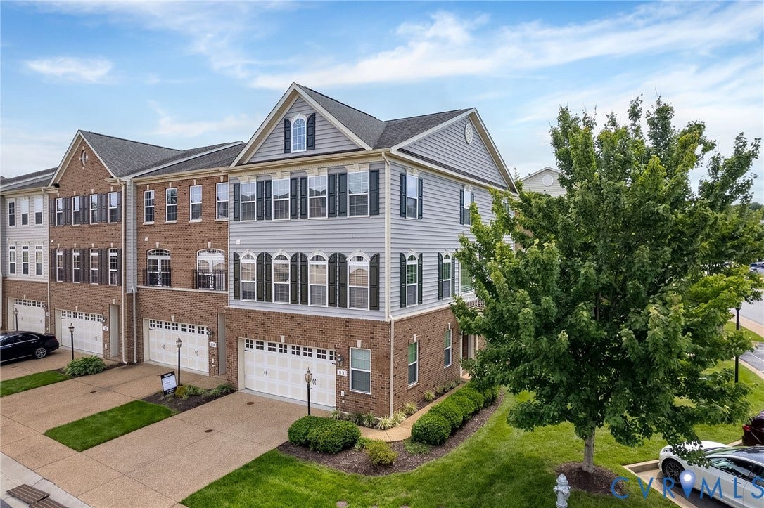 Three-story townhome featuring brick and siding exterior, multiple gables, arched windows, and an attached two-car garage