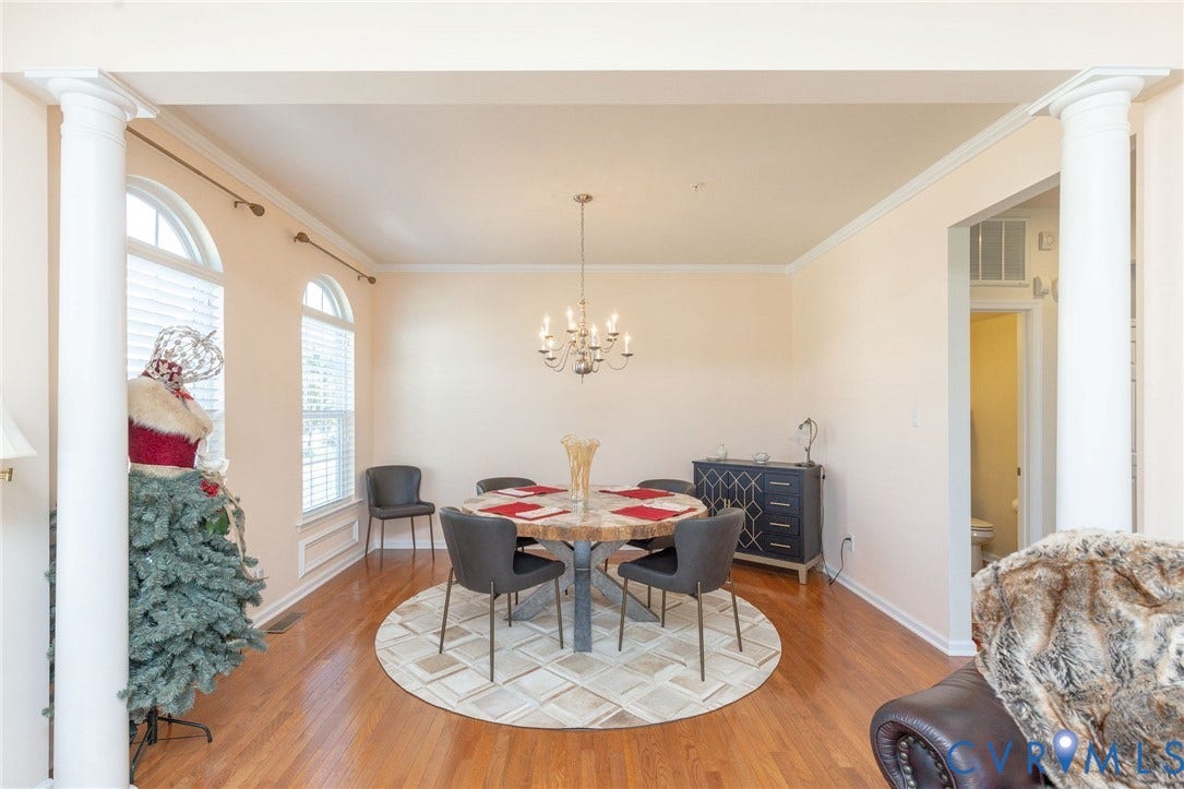 Hardwood flooring, arched window details, prominent columns, crown molding, and a chandelier lighting fixture