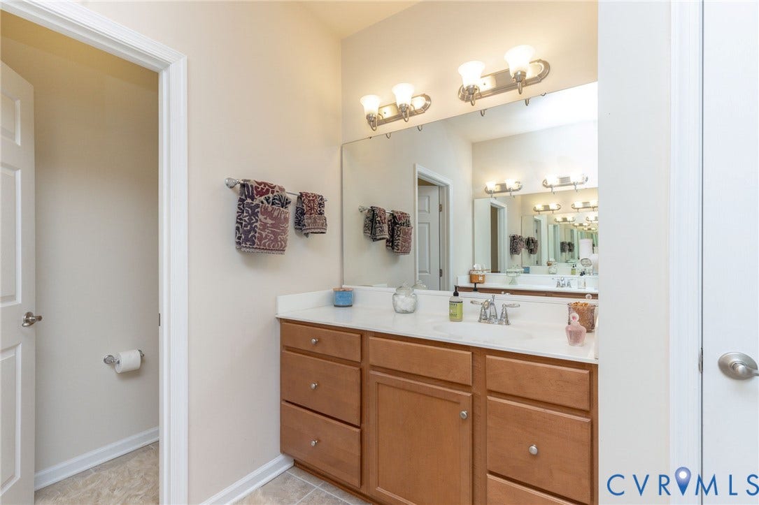 Double vanity with light wood-finish cabinetry, white countertop, and dual wall-mounted light fixtures