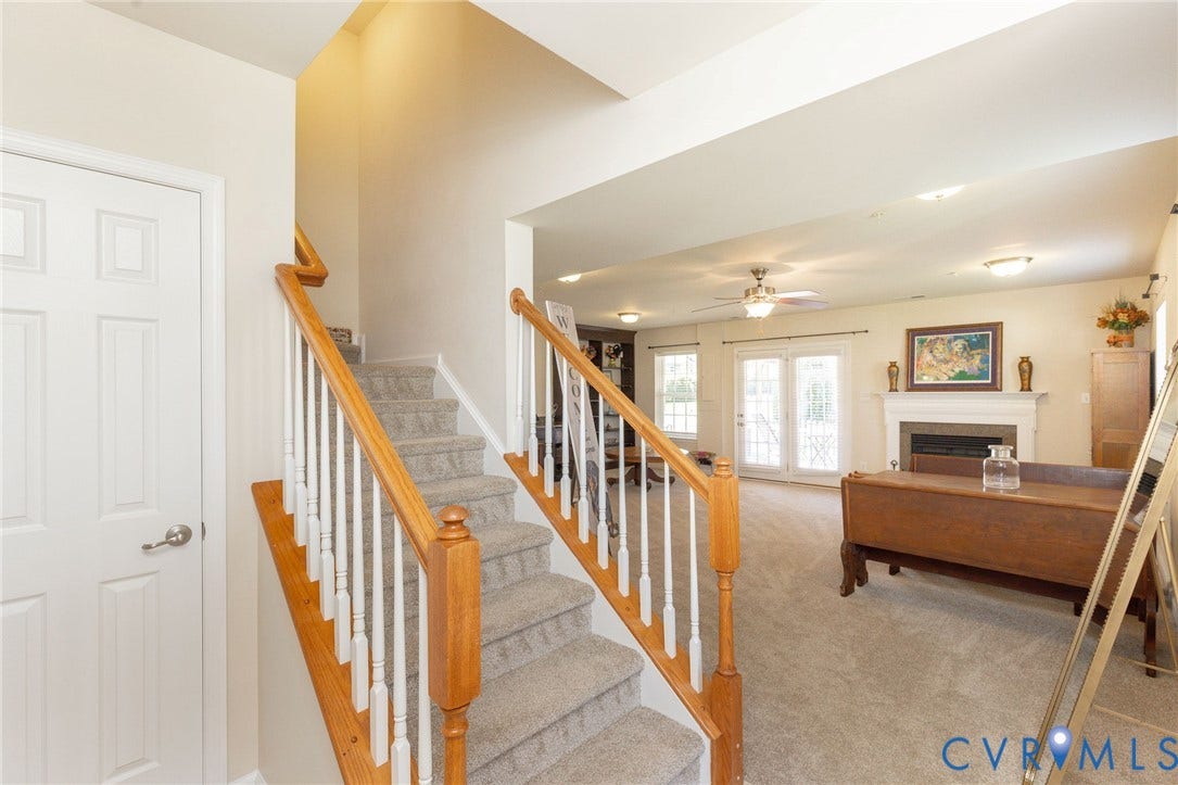 Carpeted stairs with wood handrails, a living space with a fireplace, and French doors