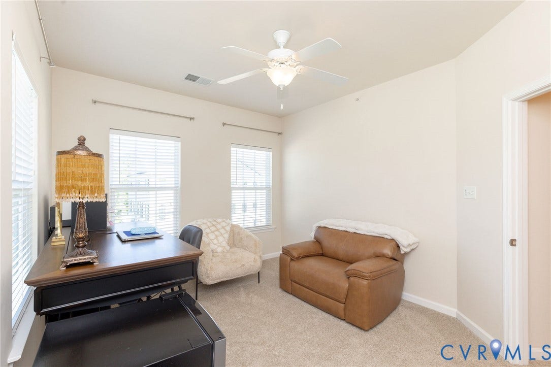 Wall-to-wall carpeting, multiple windows with blinds, a ceiling fan with integrated lighting, and a white interior door