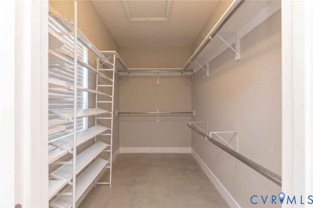 Walk-in closet with integrated shelving, multiple hanging rods, and a window with horizontal blinds