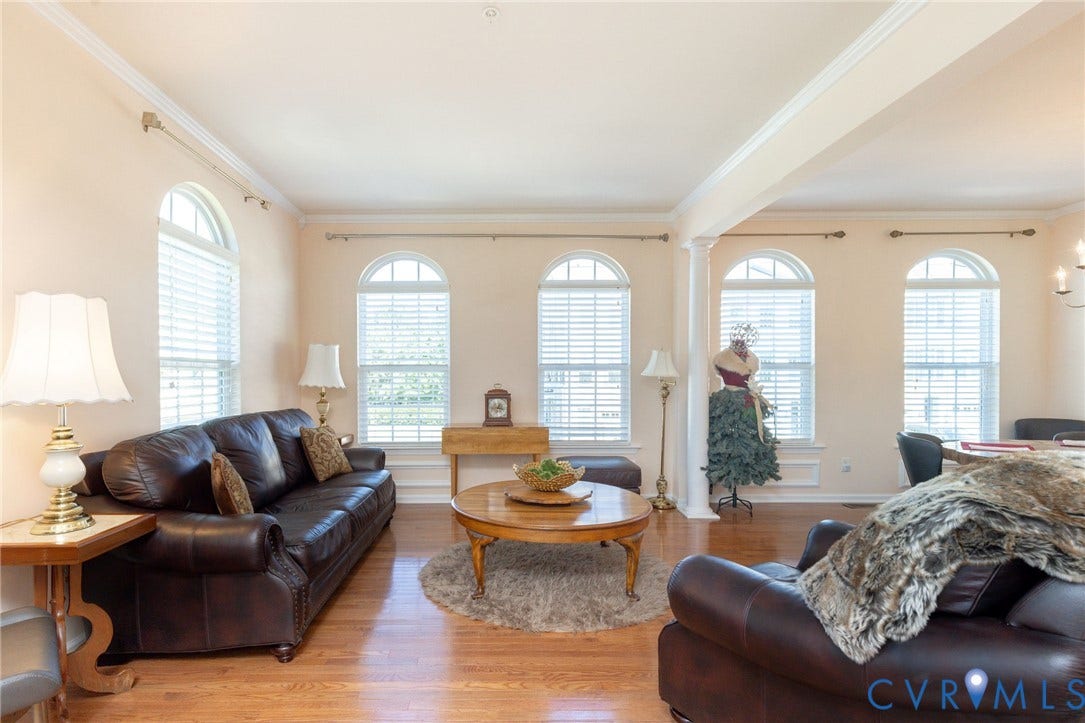 Wood-finish flooring, crown molding, and multiple arched windows with blinds