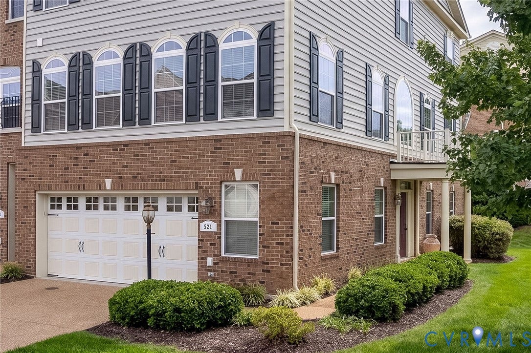 Brick and siding facade with a two-car garage, arched windows, and a covered entry