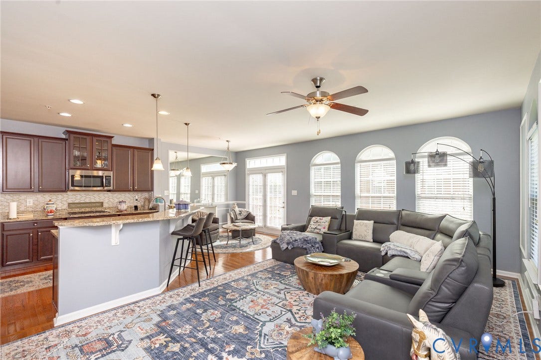 Open-concept living space featuring wood-finish flooring, a kitchen island with pendant lighting, dark wood cabinetry, and stainless steel appliances