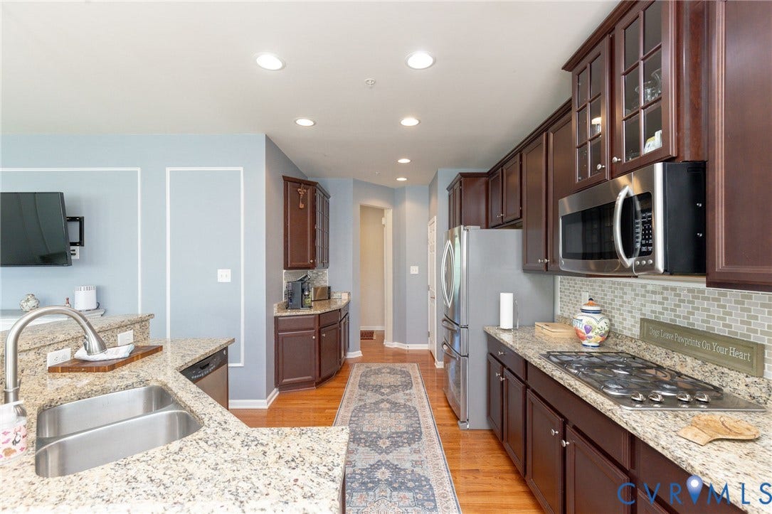 Kitchen featuring rich wood cabinetry, stainless steel appliances, granite countertops, a double basin sink, and a tile backsplash