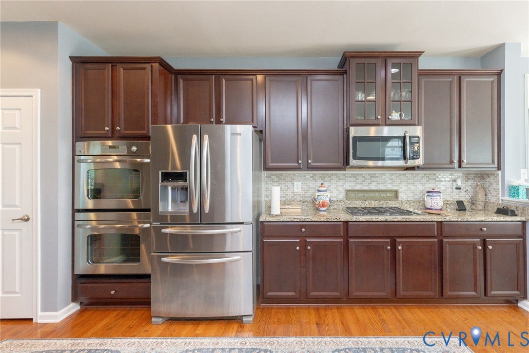 Cherry wood-finish cabinetry, stainless steel appliances, dual built-in ovens, a gas cooktop, and granite countertops