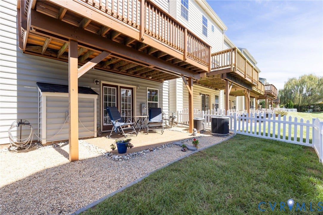 Ground-level patio with double glass doors, white picket fence, gravel pathway, and a detached storage shed
