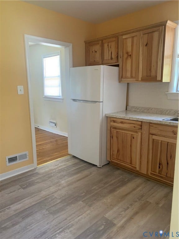 Kitchen featuring wood-finish flooring, wood cabinetry, light-toned countertops, and a white refrigerator