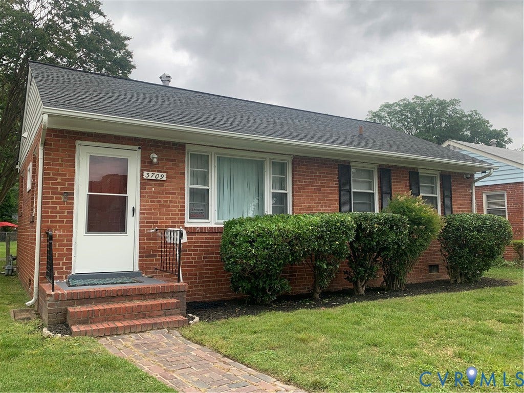 Brick exterior with a dark shingle roof, white trim, and black shutters