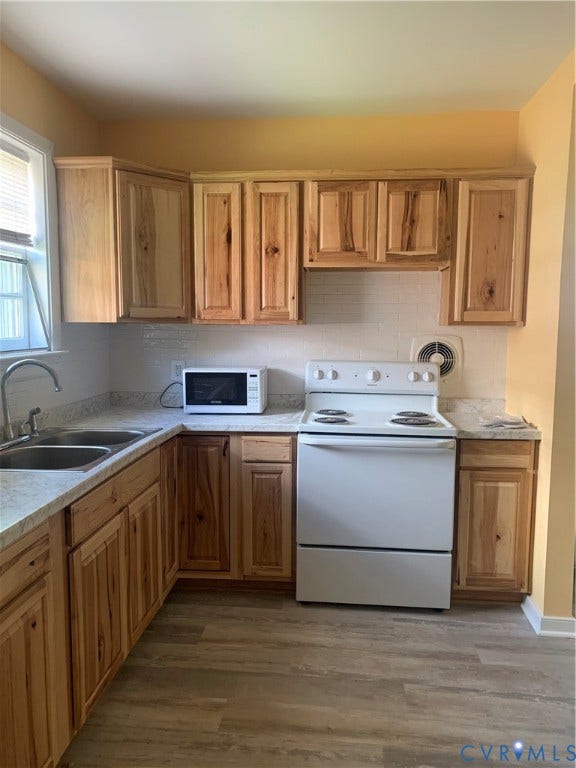 Kitchen featuring wood-finish cabinetry, light-toned countertops, a stainless steel double sink, and wood-finish flooring