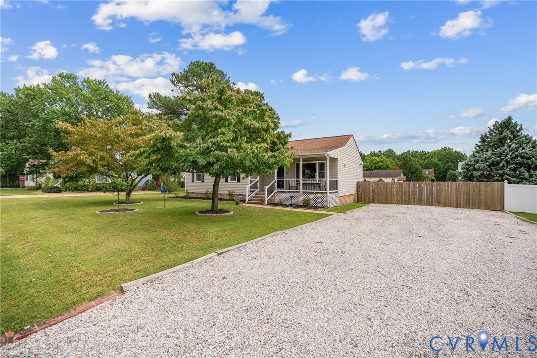 Expansive gravel driveway, manicured lawn with mature trees, screened porch, and a wood privacy fence
