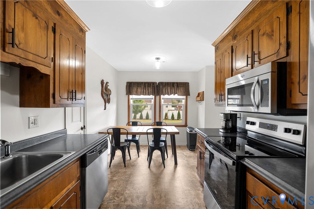 Kitchen featuring wood cabinetry with dark hardware, dark countertops, stainless steel appliances, and wood-finish flooring