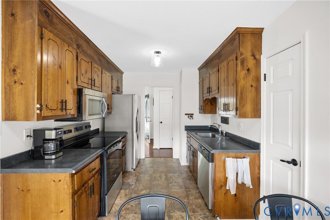 Galley kitchen featuring wood cabinetry, dark countertops, stainless steel appliances, and tile flooring