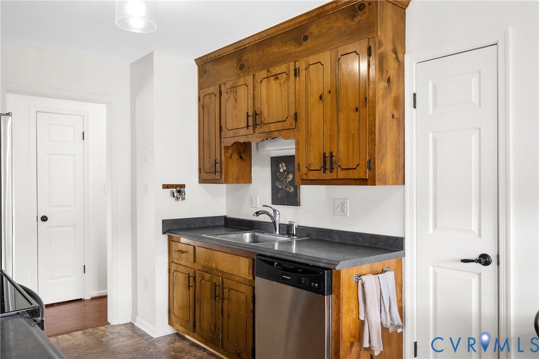 Kitchen featuring wood-finish cabinetry, a stainless steel dishwasher, a double basin sink, and dark countertops