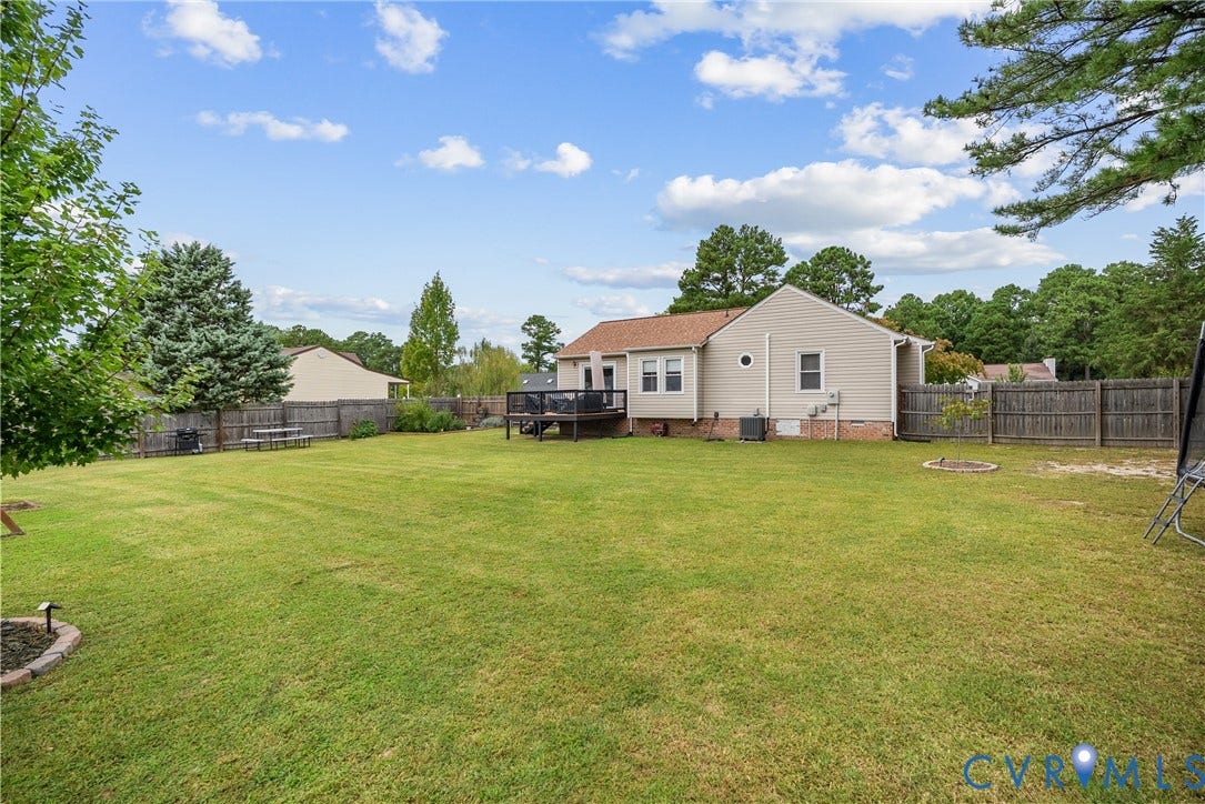 Expansive backyard featuring a lush lawn, privacy fencing, and a raised wood deck