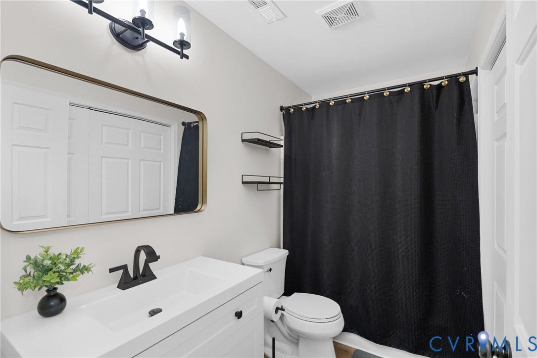 White vanity with an integrated sink and matte black faucet, framed mirror with rounded corners, and a two-light vanity fixture