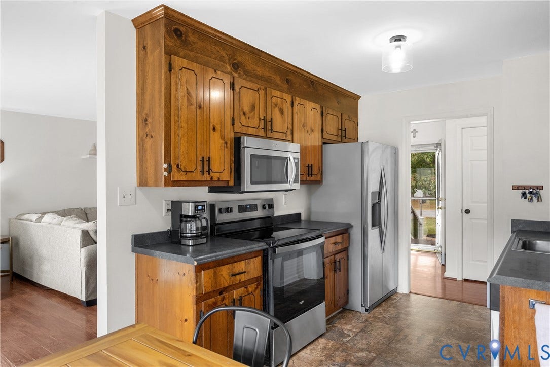 Kitchen with wood cabinetry, stainless steel appliances, dark countertops, and vinyl flooring