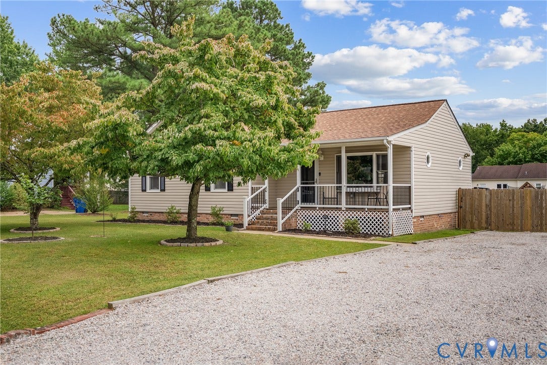 Siding exterior with a covered front porch, gravel driveway, and a fenced side yard
