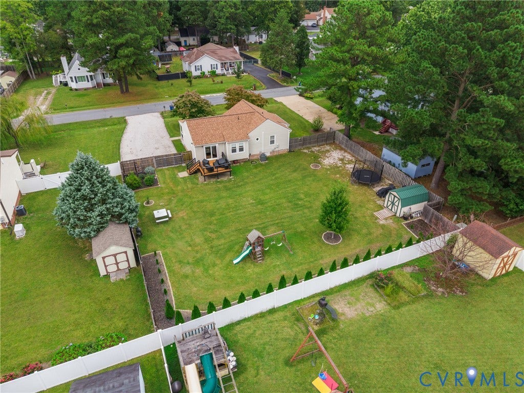 Expansive backyard featuring a manicured lawn, multiple storage sheds, a privacy fence, and a gravel driveway