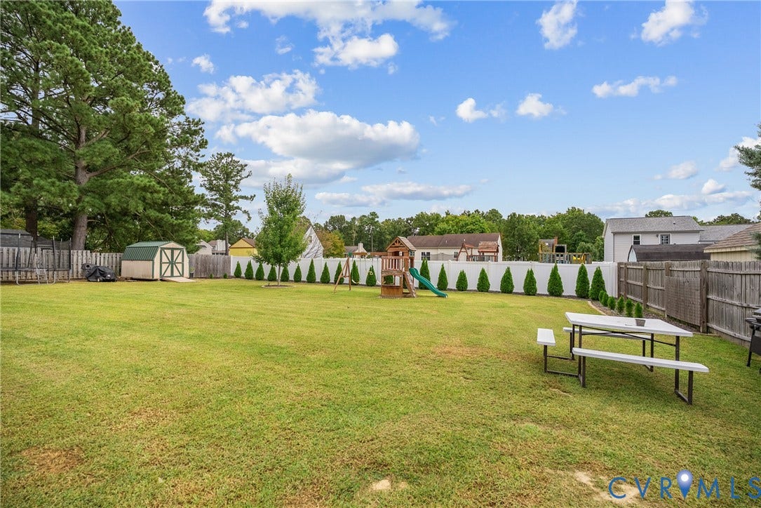 Expansive green lawn with a privacy fence, mature trees, and a storage shed