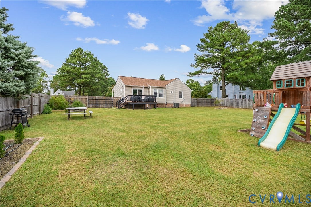 Expansive backyard featuring a privacy fence, a wooden deck, and mature trees