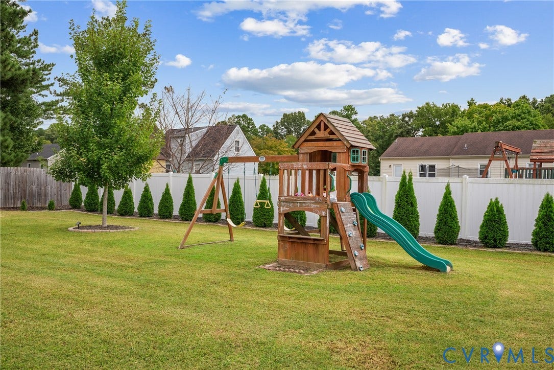 Expansive green lawn with a white privacy fence, mature trees, and landscaping
