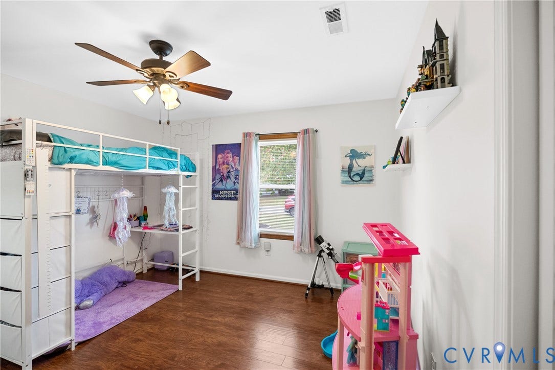 Wood-finish flooring, white walls, window with wood trim, ceiling fan with integrated lighting, and a white floating wall shelf