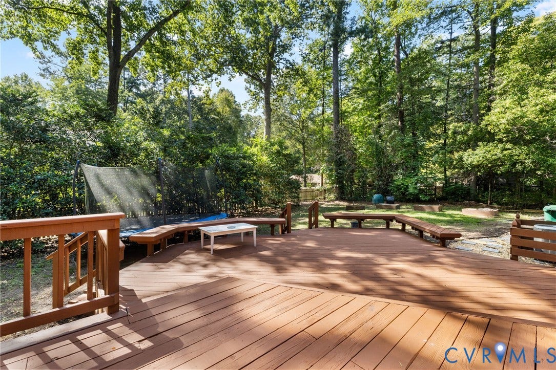 Expansive wood deck with integrated seating, surrounded by mature trees, offering ample outdoor living space