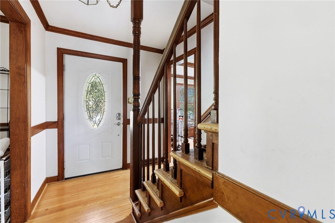 Hardwood flooring, wood trim, white entry door with decorative glass insert, and wood staircase with balusters