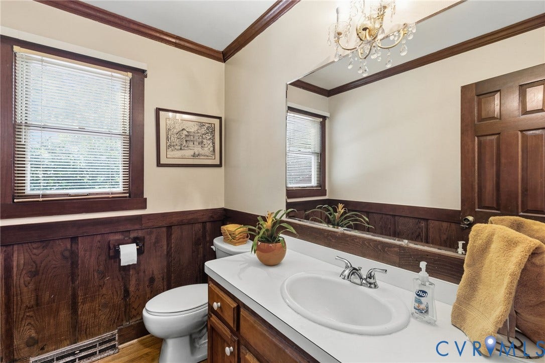 Wood-finish wainscoting, a built-in vanity with a white countertop and oval undermount sink, and a large wall-mounted mirror