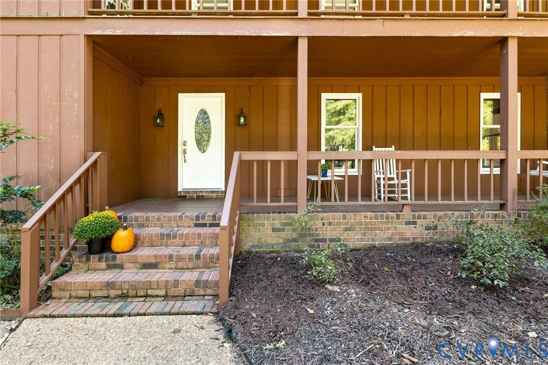 Expansive front porch featuring brick steps, wood railings, and a white front door with an oval glass insert