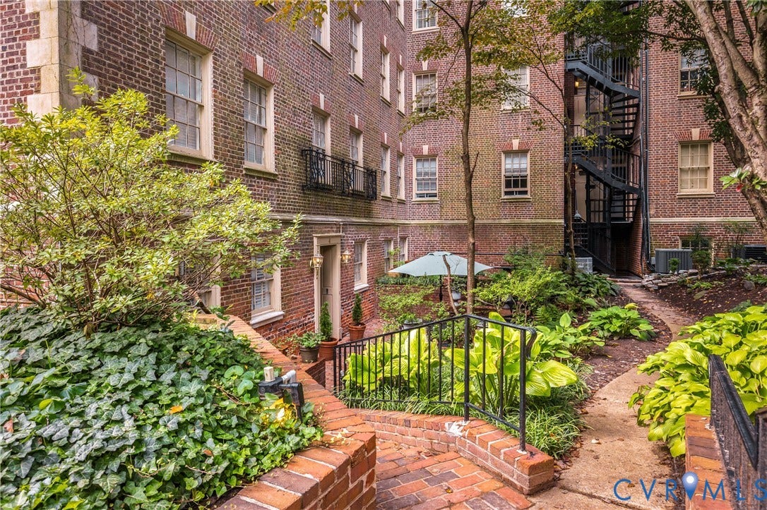 5621 Cary Street Road, #U4, Wilton, Richmond, VA 23226 Classic brick exterior featuring a multi-story layout, wrought iron fire escape, decorative masonry detailing, a stone-paved walkway, and landscaped garden beds