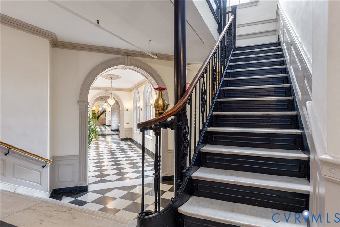 5621 Cary Street Road, #U4, Wilton, Richmond, VA 23226 Staircase featuring black iron railings, a wood handrail, and stone-tread steps, complemented by arched entryways, crown molding, and a checkered stone floor pattern