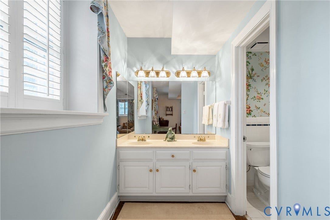5621 Cary Street Road, #U4, Wilton, Richmond, VA 23226 Double vanity featuring white cabinetry, a solid surface countertop with integrated dual sinks, a full-width vanity mirror, and multi-bulb wall-mounted lighting