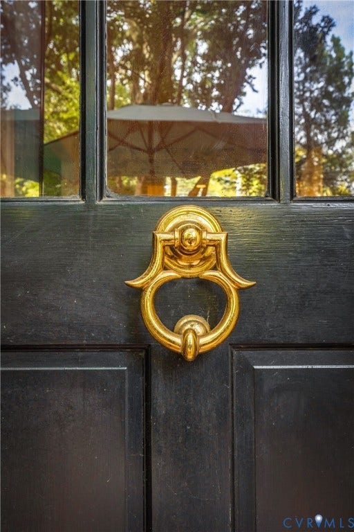 5621 Cary Street Road, #U4, Wilton, Richmond, VA 23226 Elegant black double doors featuring ornate brass ring hardware and upper glass panels, framed by mature trees visible through the glazing