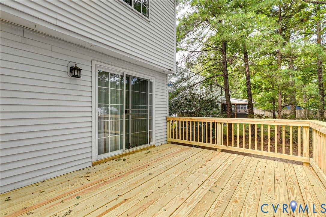 Spacious wood deck with a natural finish, featuring a full wood railing, sliding glass door access, exterior wall lantern, and light-colored siding