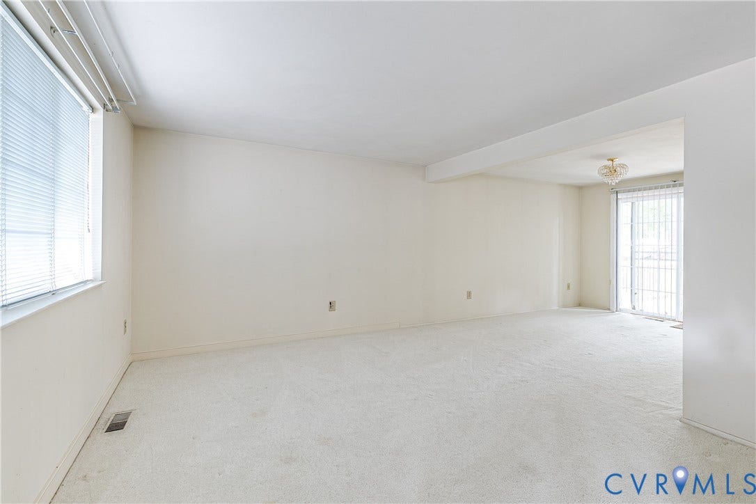 Carpeted room with a large window featuring horizontal blinds and a sliding glass door