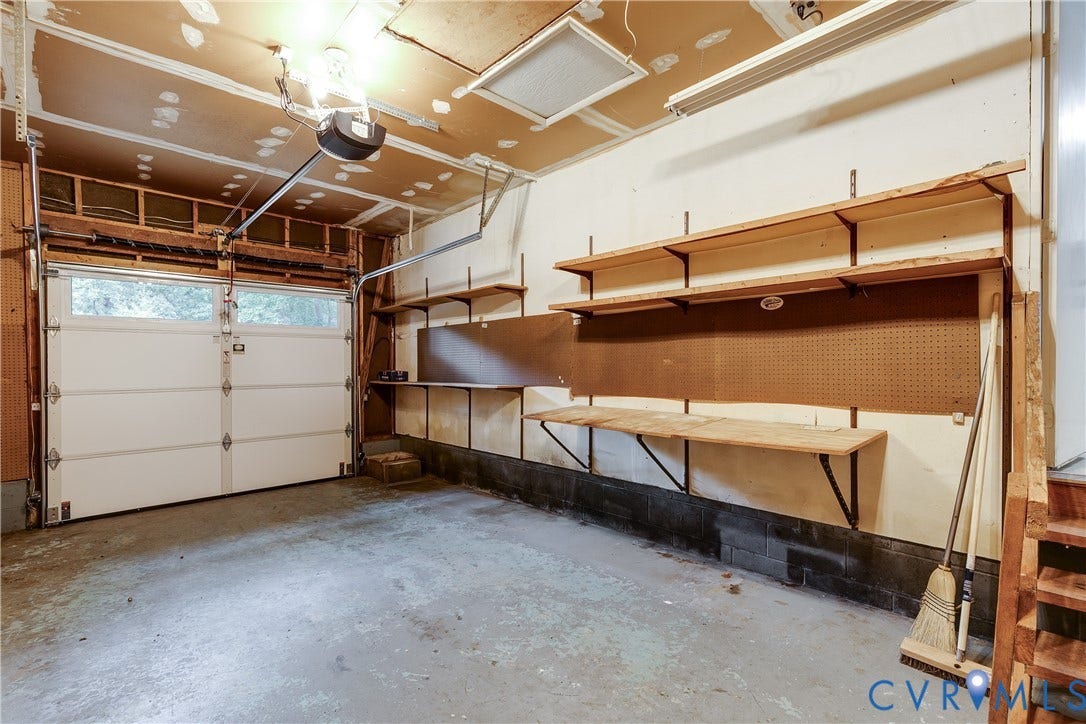 Attached garage with overhead door, built-in shelving, pegboard, and concrete flooring