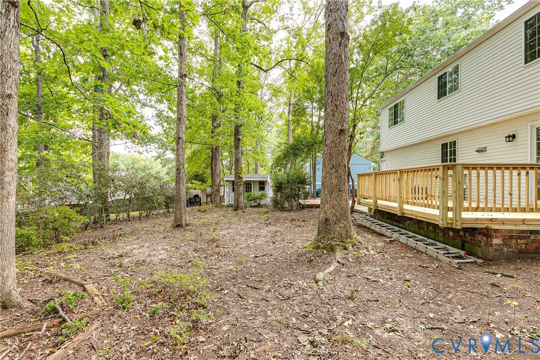 Expansive yard featuring mature trees, a wood deck, white siding, and a detached shed