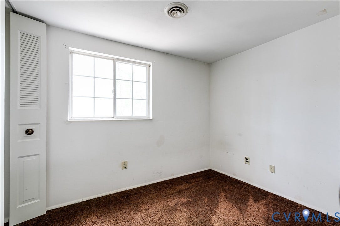 White walls with brown carpeting, featuring a multi-pane window and a louvered bi-fold door