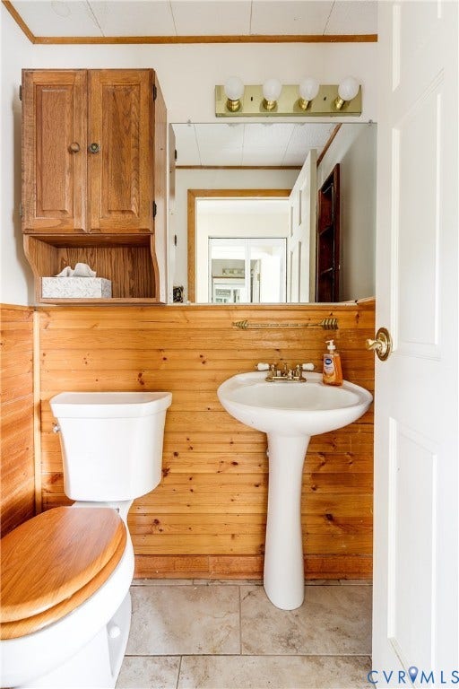 Pedestal sink with brass-finish faucet, wall-mounted medicine cabinet, toilet with wood-finish seat, tiled flooring, and wood paneling
