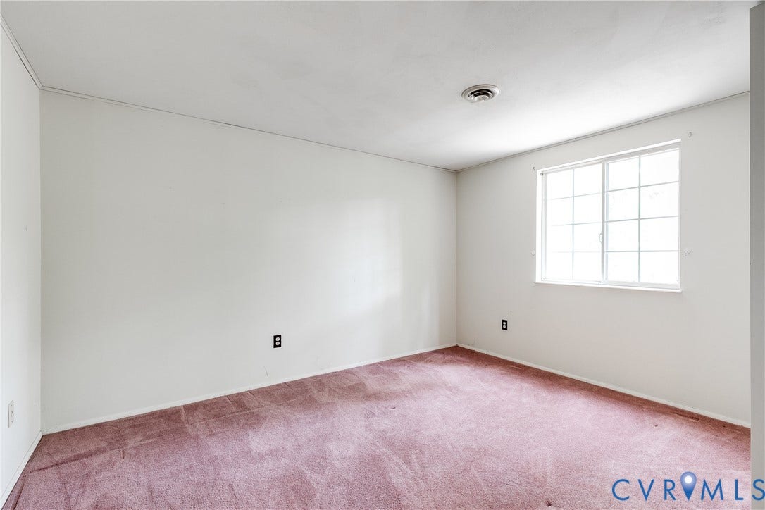 White painted walls, pink carpeting, and a single window with gridded panes