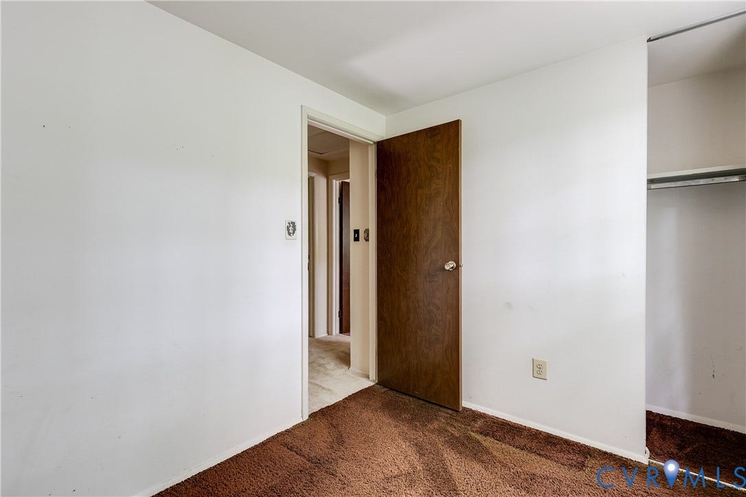 Textured brown carpeting with white painted walls, a wood-finish door, and an open closet with a metal hanging rod