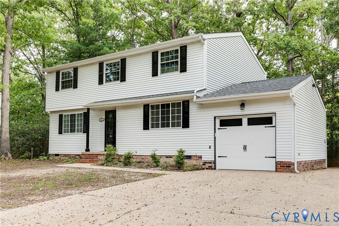 White siding exterior with black shutters, attached single-car garage, brick foundation, and a light-colored driveway